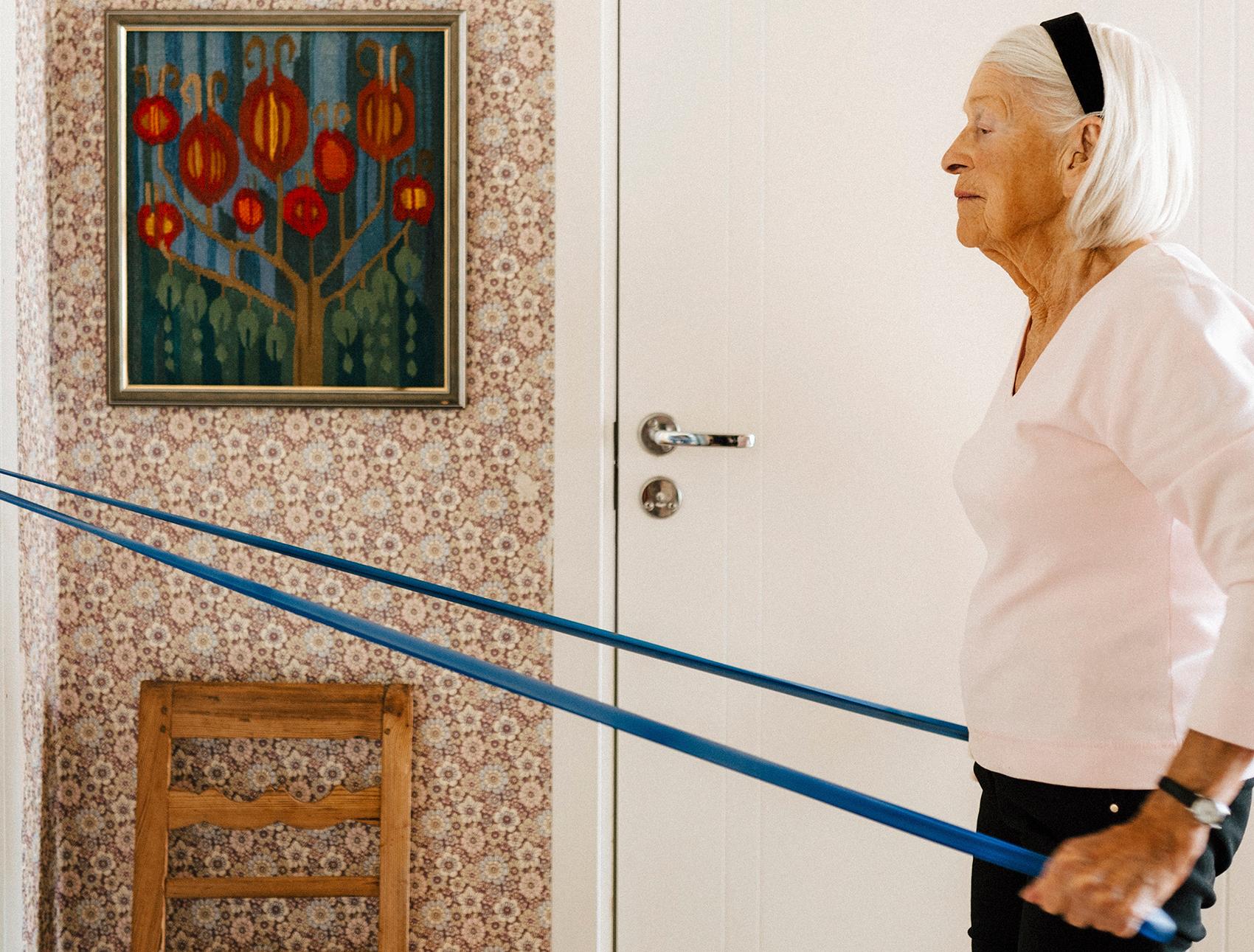 Äldre kvinna som tränar med gummiband i sitt hem.